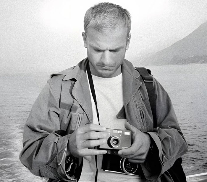 Black and white photo of a VF photographer holding a camera near the sea, relating to Karoline Leavitt close-up defense.