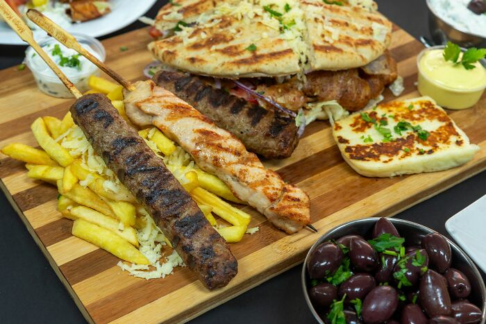Grilled Greek skewers, fries, pita bread, olives, and cheese served on a wooden platter in a Greek village meal setting