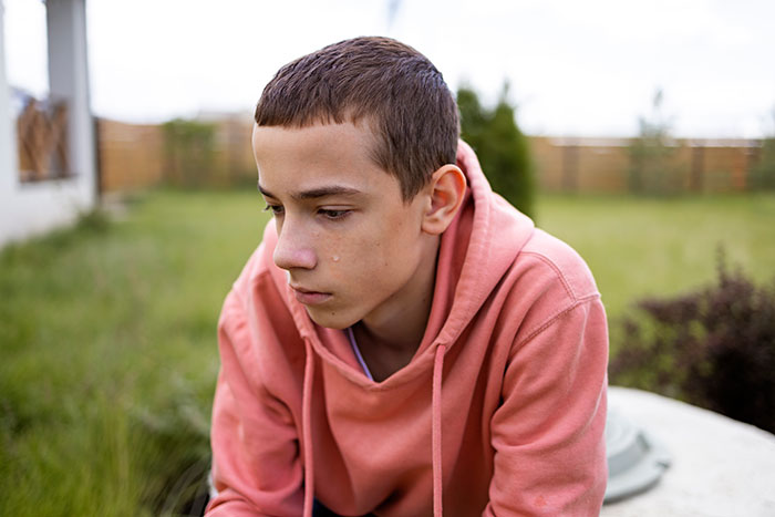 Exhausted teen in pink hoodie sitting outdoors, tear on cheek, looking sleepless and distressed Exhausted teen in pink hoodie sitting outdoors, tear on cheek, looking sleepless and distressed