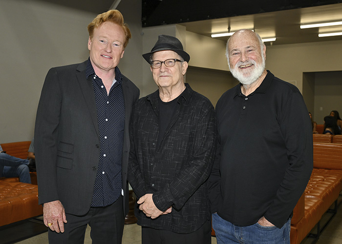 Conan O&rsquo;Brien with two men at an event, posing for a photo in a room with leather seating and industrial lighting.