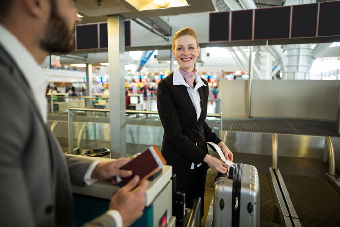 Airline worker smiling at passenger while handling luggage at airport counter amid luggage policy dispute.