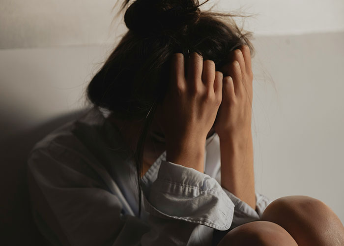Stressed woman holding head in hands in dim light, reflecting tension related to closet door argument and public clap back.