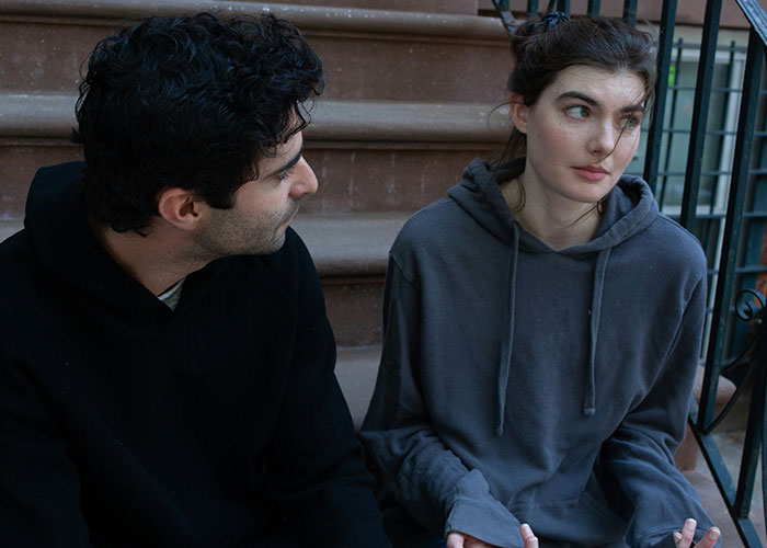 Couple sitting on outdoor steps, woman looking upset while man talks, reflecting a relationship conflict online.