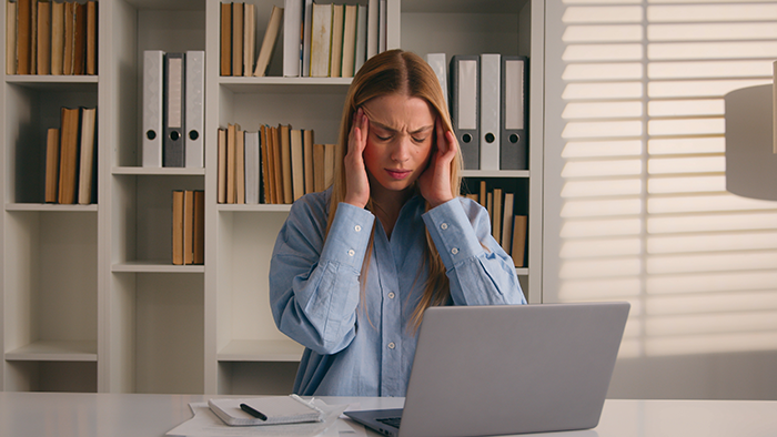 Frustrated woman at laptop holding her head, depicting a coworker refusing to fix her own mistake during a call. Frustrated woman at laptop holding her head, depicting a coworker refusing to fix her own mistake during a call.