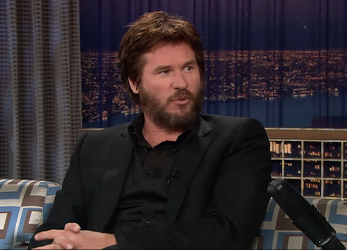 Actor with beard and dark hair wearing black suit talking during late night celebrity interview show.