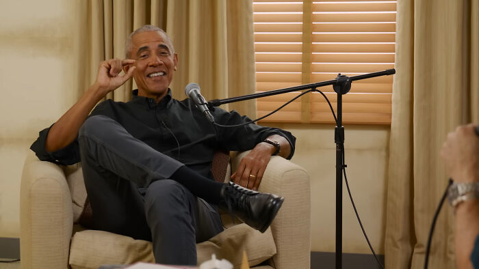 Former US president in casual black outfit sharing stories during a relaxed celebrity encounter podcast recording.