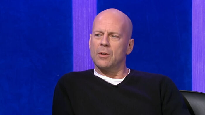 Bald man in a black sweater sitting against a blue background, captured during a celebrity encounter discussion.