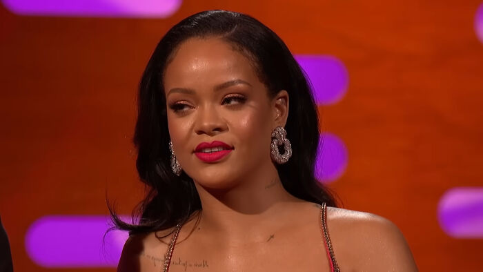 Celebrity encounter with Rihanna wearing statement earrings and red lipstick on a brightly lit TV show set.