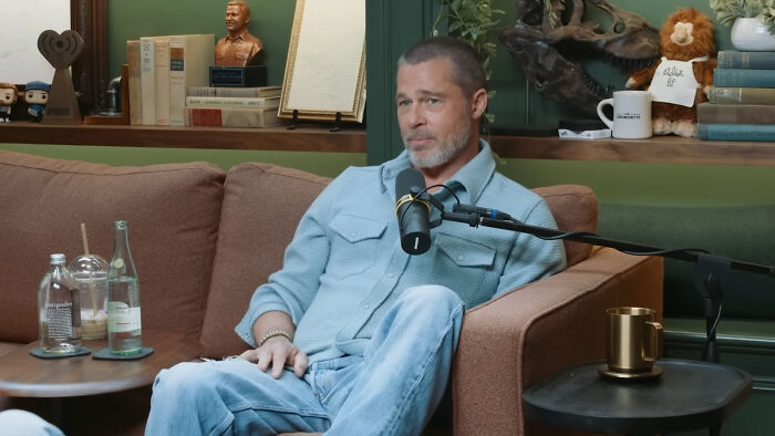 Man casually sitting on couch talking into microphone during celebrity encounter podcast episode recording.
