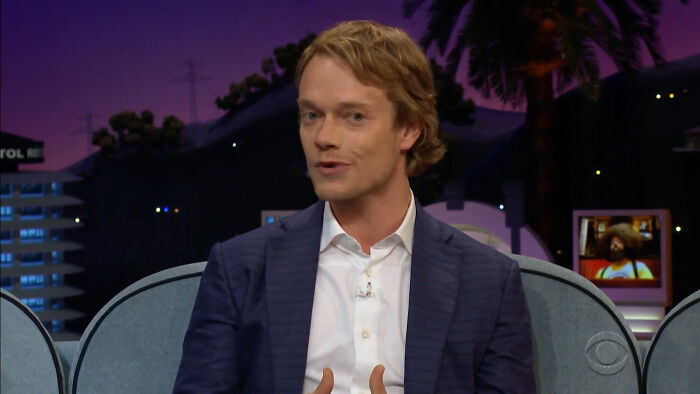 A man in a navy blazer and white shirt sharing a story about running into different celebrities on a talk show.