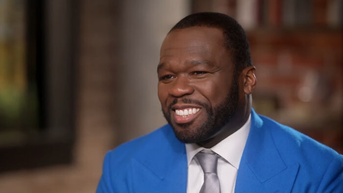 A smiling man in a bright blue suit sharing a story about ran into different celebrities in an indoor setting.