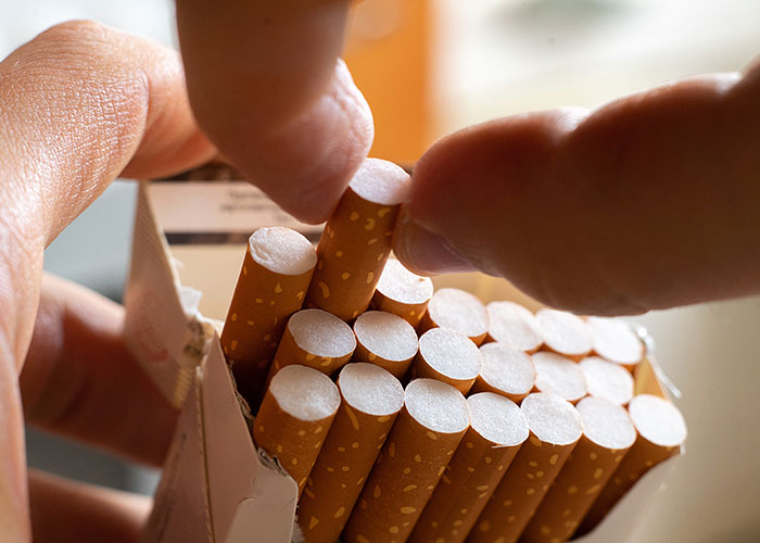 Close-up of hands picking cigarettes from an open pack illustrating concepts of poisoning or harmful acts.