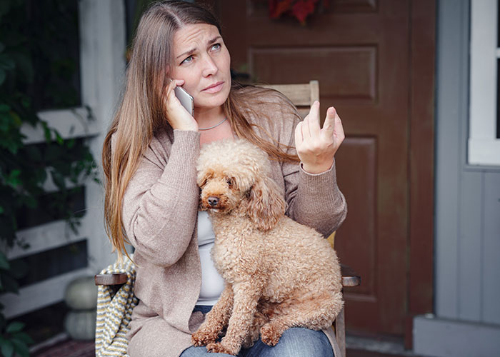 Woman on phone looking upset, holding curly dog, depicting MIL poisoning family dog and verbal attack situation.