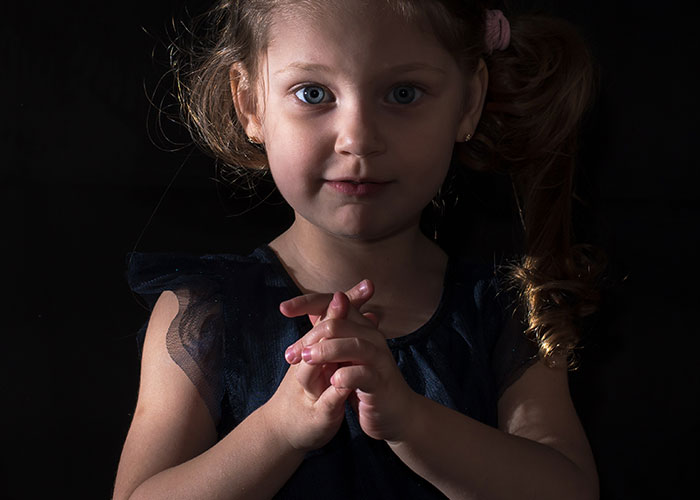 Young girl with a mysterious expression in low light, illustrating creepy things kids said that scared their parents.