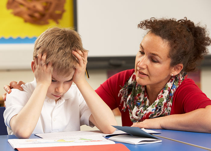 Woman comforting a distressed child at a school desk, illustrating creepy things kids said that scared their parents.