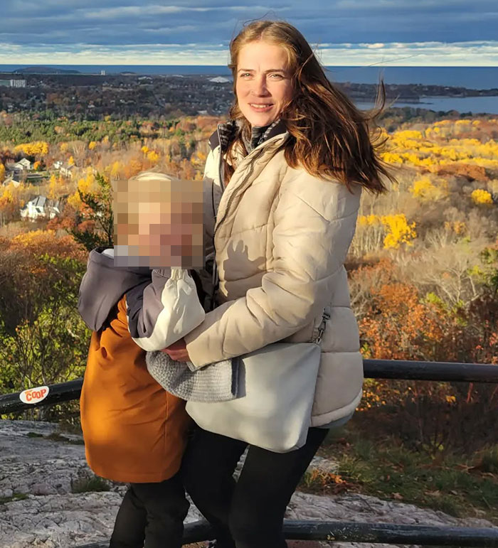 Woman in beige jacket holding child with blurred face outdoors in autumn landscape related to racist Cinnabon worker news. Woman in beige jacket holding child with blurred face outdoors in autumn landscape related to racist Cinnabon worker news.