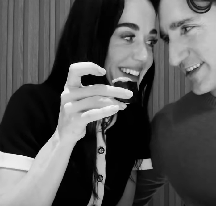 Katy Perry smiling while holding a piece of sushi, engaging warmly with Justin Trudeau in a casual setting.