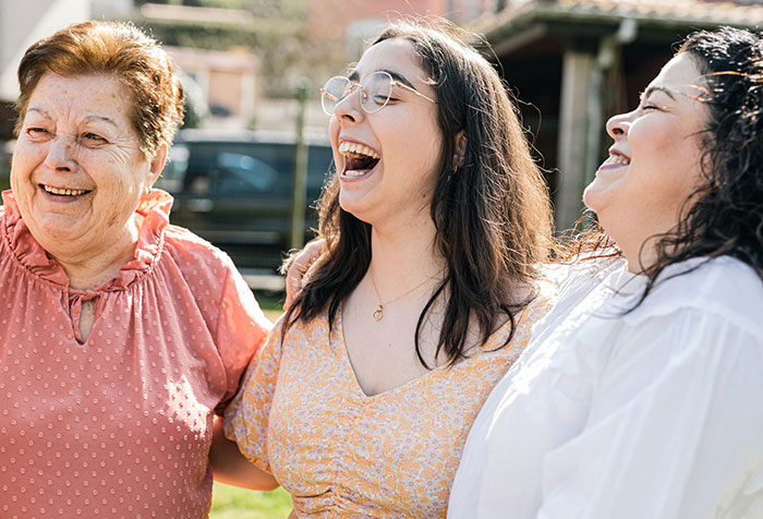 Three women laughing together outdoors, capturing a moment of joy related to rich aunt and petty Christmas revenge.
