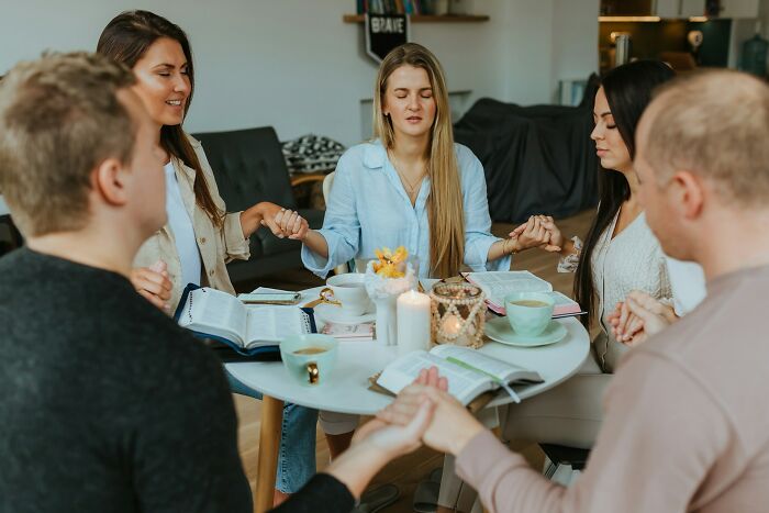 Group of young adults holding hands and reflecting together around a table, highlighting harmless but toxic habits discussion.