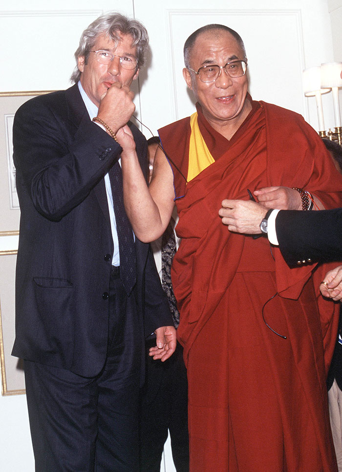 Richard Gere in a suit standing next to a man in traditional red and yellow robes during a casual event.