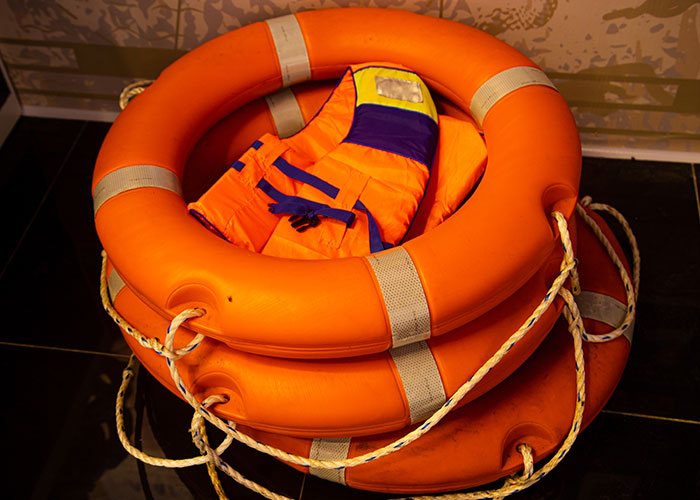 Stack of orange life rings with a bright orange life jacket inside, illustrating survival hacks and safety equipment risks.