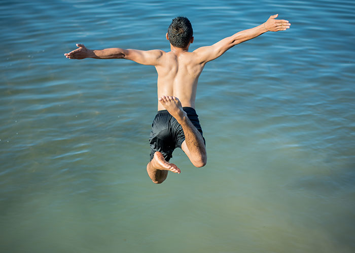 Boy in black shorts jumping into a lake, illustrating survival hacks that are useless and potentially dangerous risks.