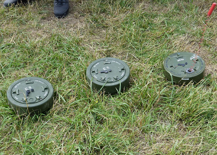 Three green landmines placed on grass with a person's feet nearby illustrating dangerous survival hacks.