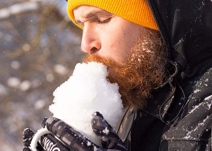 Man with a beard wearing a yellow hat and black jacket eating snow outdoors, illustrating survival hacks that can be dangerous.
