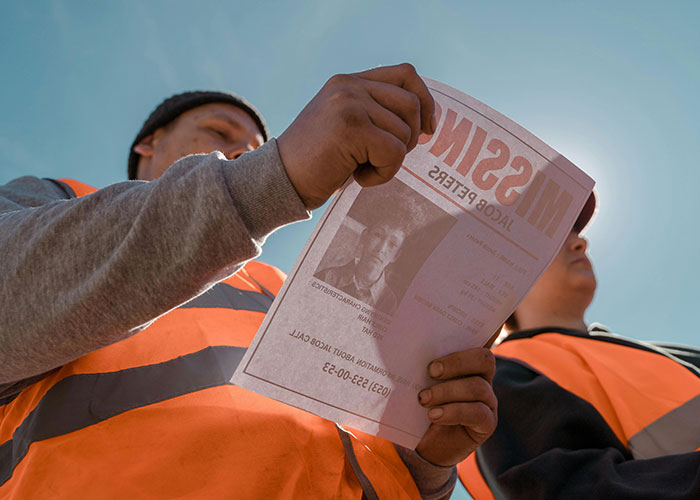 Two men in orange safety vests examining a missing person flyer, illustrating survival hacks that can be dangerous.