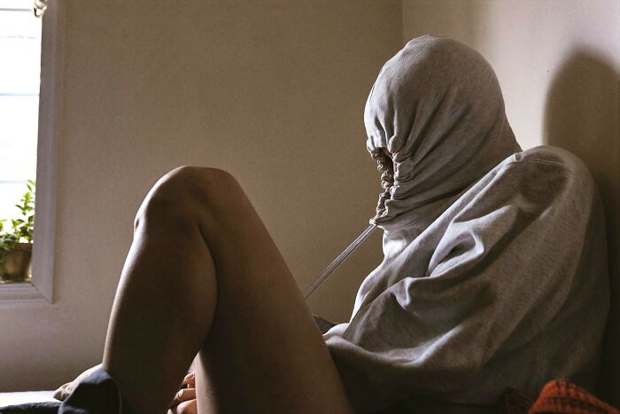 Person sitting with hoodie tightened over their face in a dim room, illustrating unusual and surprising life facts.