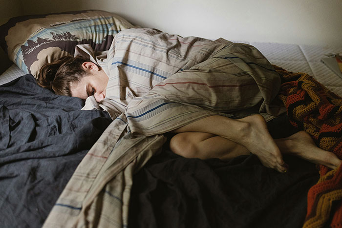 Woman wrapped in blanket lying on bed, reflecting exhaustion and frustration during Thanksgiving with brother-in-law tensions.