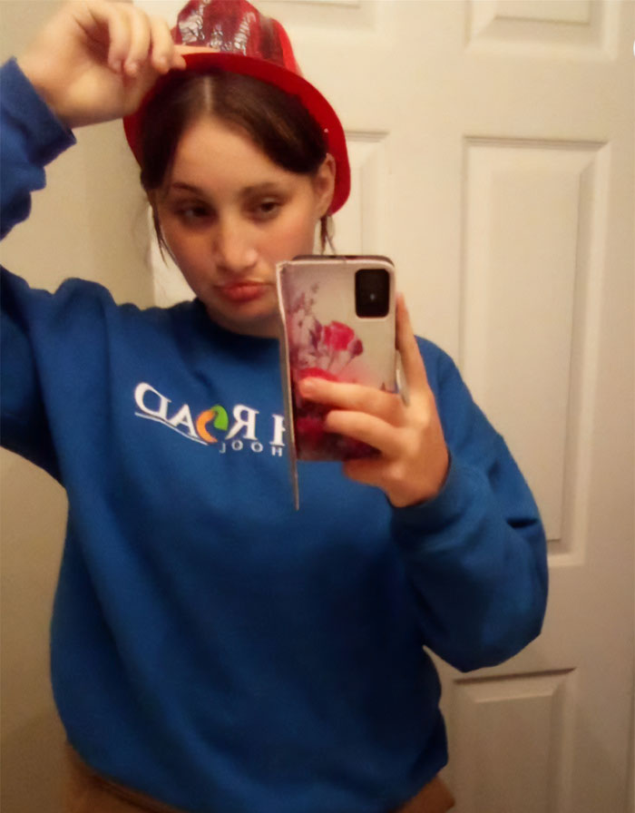Teen girl wearing a blue sweatshirt and red hat taking a mirror selfie related to revenge for getting feelings hurt case.