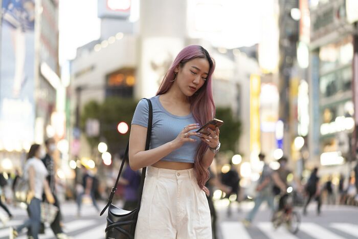 Young woman with pink hair using phone in busy city street, representing people who dated outside their culture experiences.