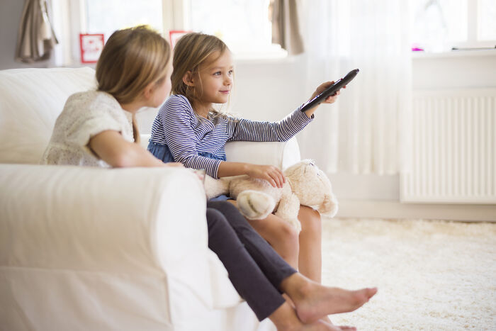 Two young girls on a white couch, one holding a remote, illustrating themes of people who dated outside of their culture.