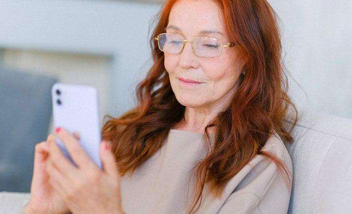 Woman with glasses sitting on a couch using smartphone, reflecting on a family issue involving gay daughter and holiday plans. Woman with glasses sitting on a couch using smartphone, reflecting on a family issue involving gay daughter and holiday plans.