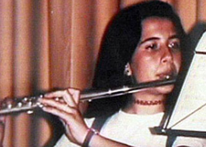 Young woman playing the flute indoors with a music stand, part of the Vatican girl cold case from decades ago.