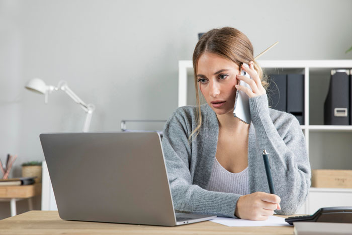 Young woman on phone looking stressed while working on laptop, symbolizing care for autistic brother and family demands. Young woman on phone looking stressed while working on laptop, symbolizing care for autistic brother and family demands.
