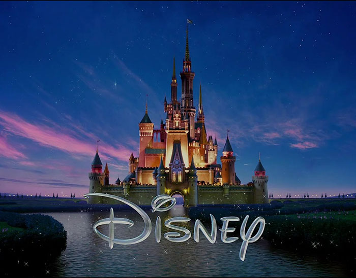 Disney castle illuminated at dusk with a reflection in water, symbolizing discussions on Disney remakes and controversy.