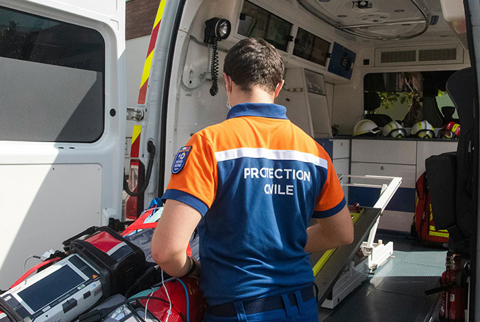 Emergency responder in a civil protection uniform preparing medical equipment inside an ambulance after a lung collapse incident.