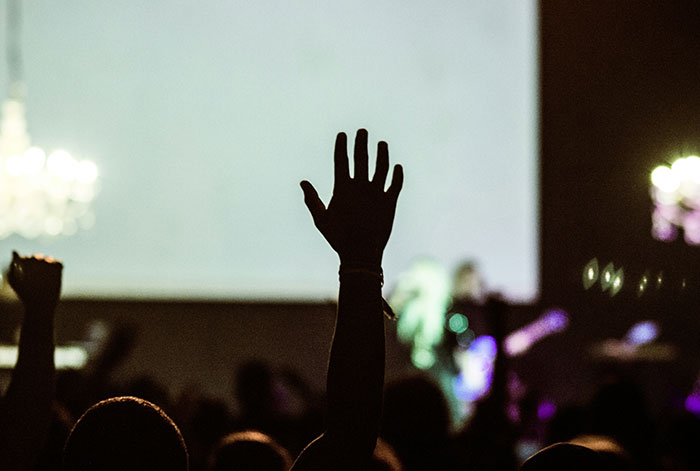 Audience member raising hand in a dark event setting, symbolizing urgent medical help and doctor intervention stories.