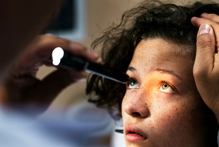 Doctor examining a young patient's eyes with a penlight during an emergency after lungs collapsed on a flight.