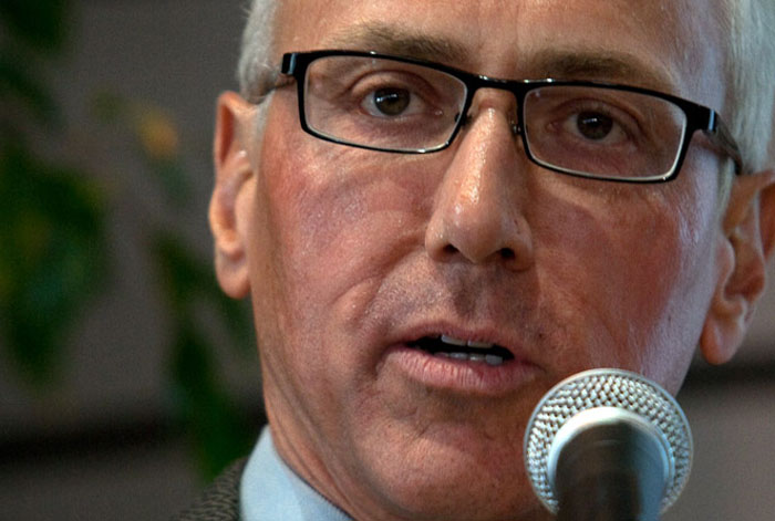 Close-up of a man wearing glasses speaking into a microphone about a medical emergency involving collapsed lungs.