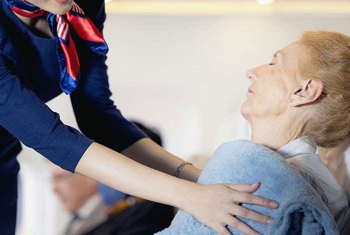 Flight attendant comforting elderly woman wrapped in a blanket during an in-flight medical emergency involving collapsed lungs.