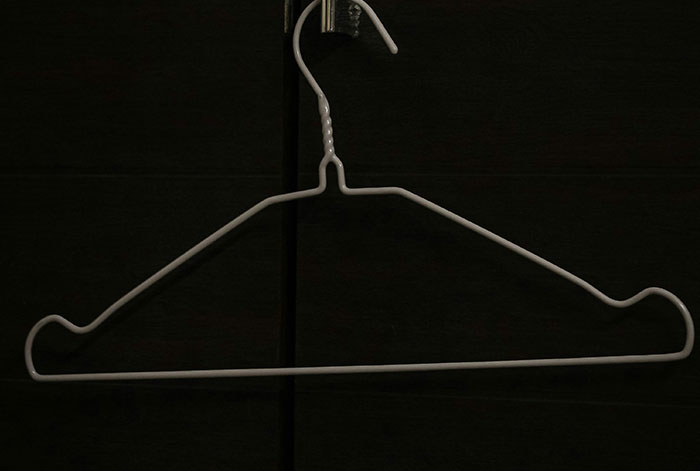 White metal clothes hanger hanging against a dark background, symbolizing emergency and medical story themes.