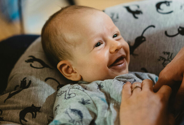 Happy baby lying on a patterned pillow, smiling while being gently held, illustrating common health concerns from doctors.