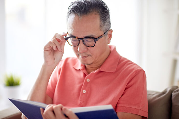 Man in a coral shirt wearing glasses and reading a book focused on common health concerns discussed by doctors.