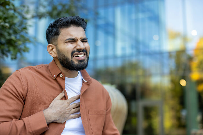 Man outdoors clutching chest with a pained expression illustrating common health concerns that freak people out but are normal