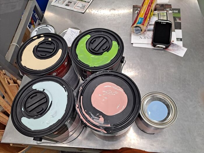 Open paint cans with pastel colors on a metal worktable, illustrating snobbish color preferences shamed online.