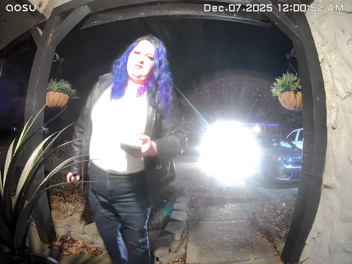 Person with blue hair standing at front door captured by porch camera with bright headlights in background at night. Person with blue hair standing at front door captured by porch camera with bright headlights in background at night.