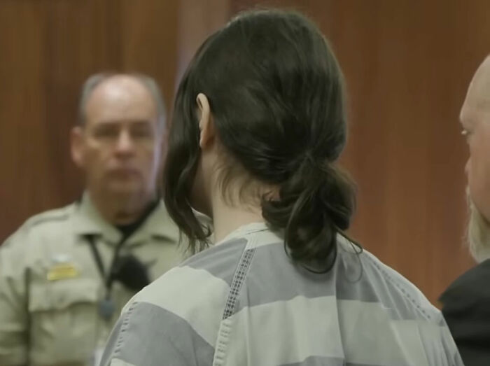 Trans Muslim woman in court wearing prison uniform during sentencing hearing with officers and legal counsel present. Trans Muslim woman in court wearing prison uniform during sentencing hearing with officers and legal counsel present.